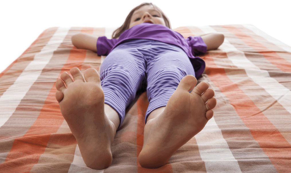 A child stretched out on a mattress, feet toward the camera